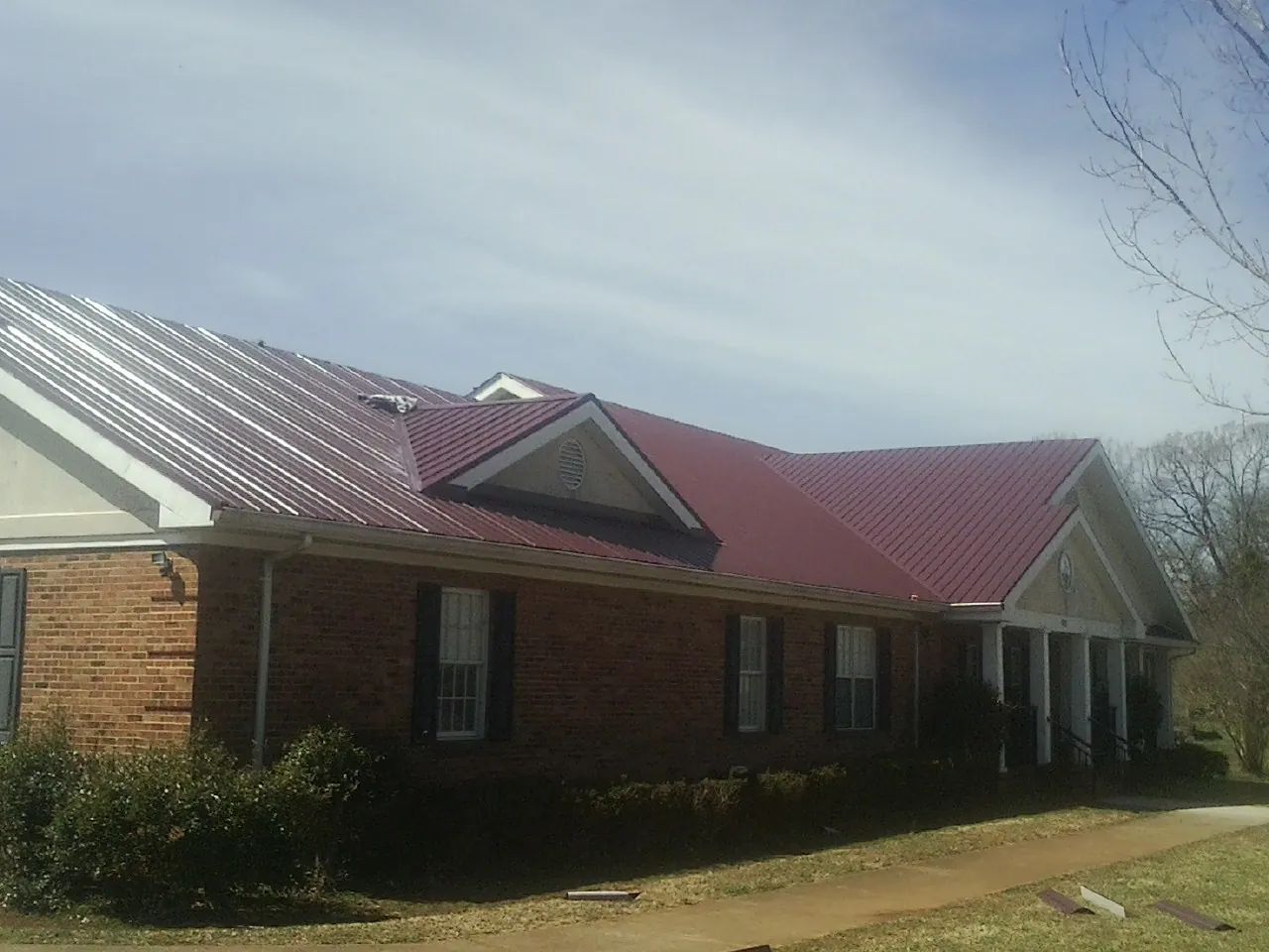 Red metal roof with gabled entries on a long brick building, from a Hail Damage Roof Repair job in Sanger