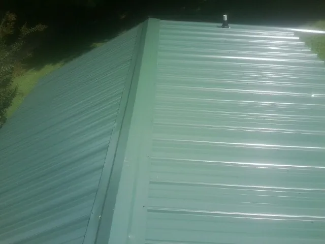 New green metal panels meeting at the ridge of a roof — Flat Roof Repair work by our crew in Sanger