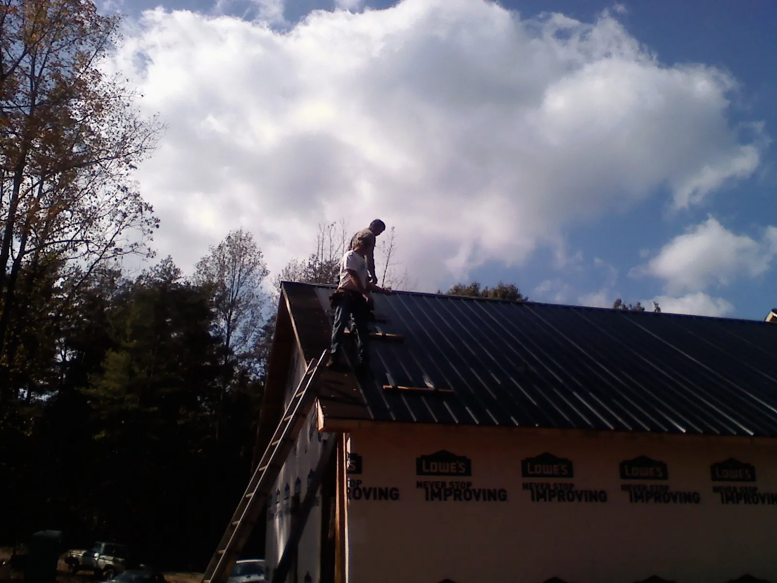 Roofer fastening dark metal panels high against a cloudy sky, from a Roof Inspection job in Sanger