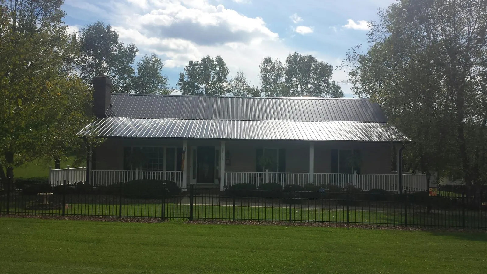 Gray metal roof on a brick ranch with a full width front porch — Gutter Guard Installation work by our crew in Sanger