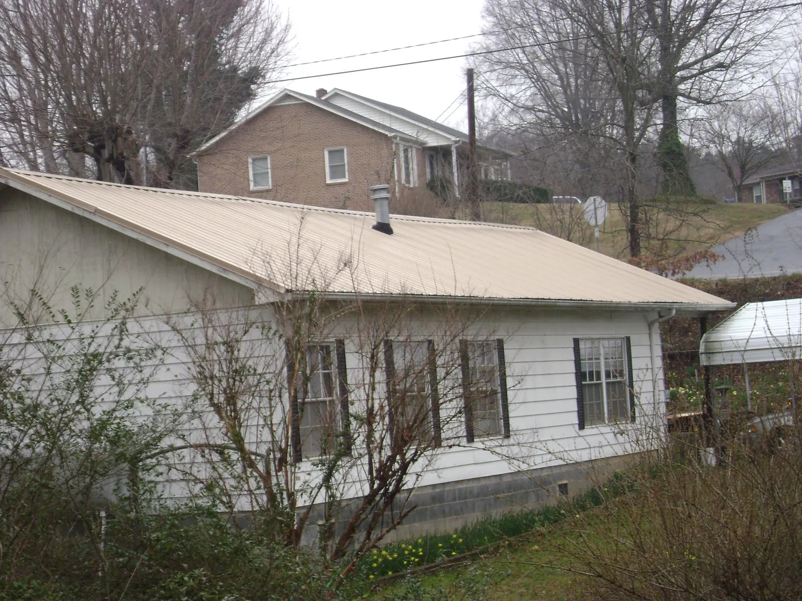 Tan metal roof on a white sided house set into a hillside — Commercial Roofing by Roofing Brothers in Sanger